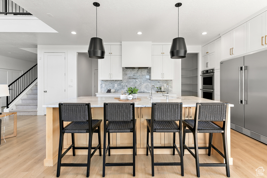 Kitchen with stainless steel appliances, light wood finished floors, backsplash, white cabinetry, and a spacious island