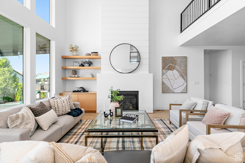 Living room featuring a towering ceiling, light wood-style flooring, and a large fireplace
