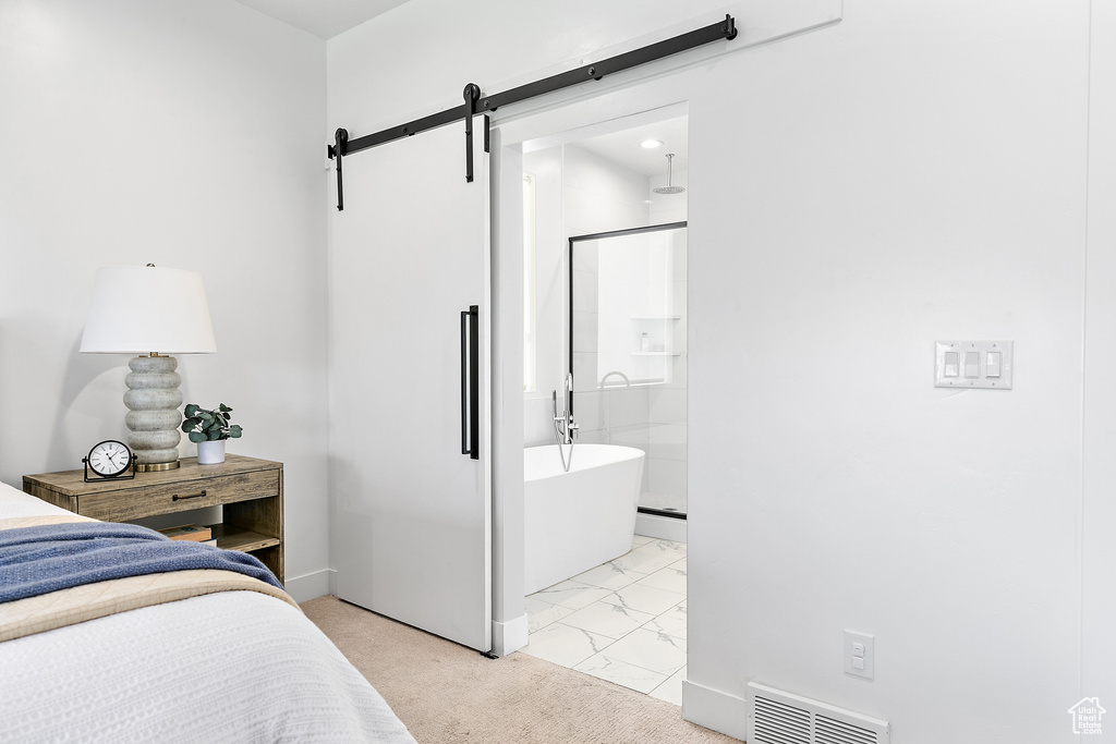 Bedroom with a barn door, light colored carpet, light marble finish floors, and connected bathroom