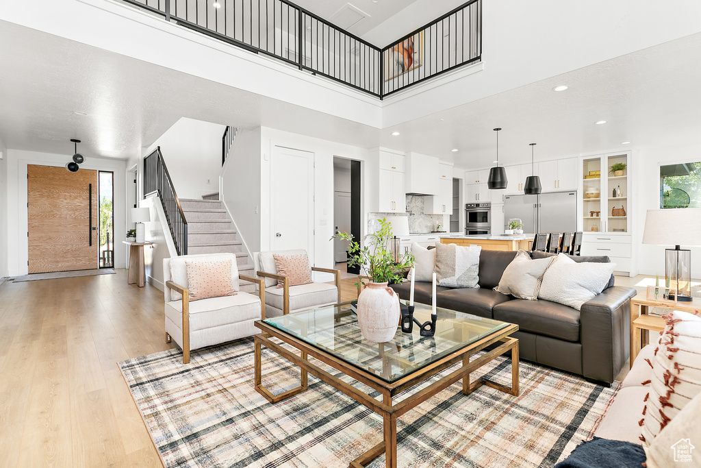 Living area with a towering ceiling, stairway, light wood-type flooring, and recessed lighting