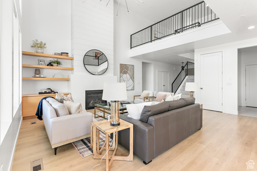 Living area with stairway, a high ceiling, light wood-type flooring, and a glass covered fireplace