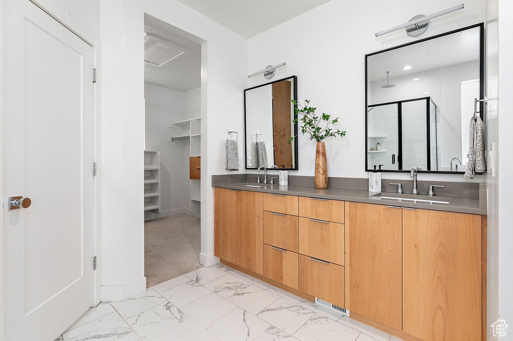 Full bathroom with marble look tiles, a shower stall, double vanity, and a spacious closet