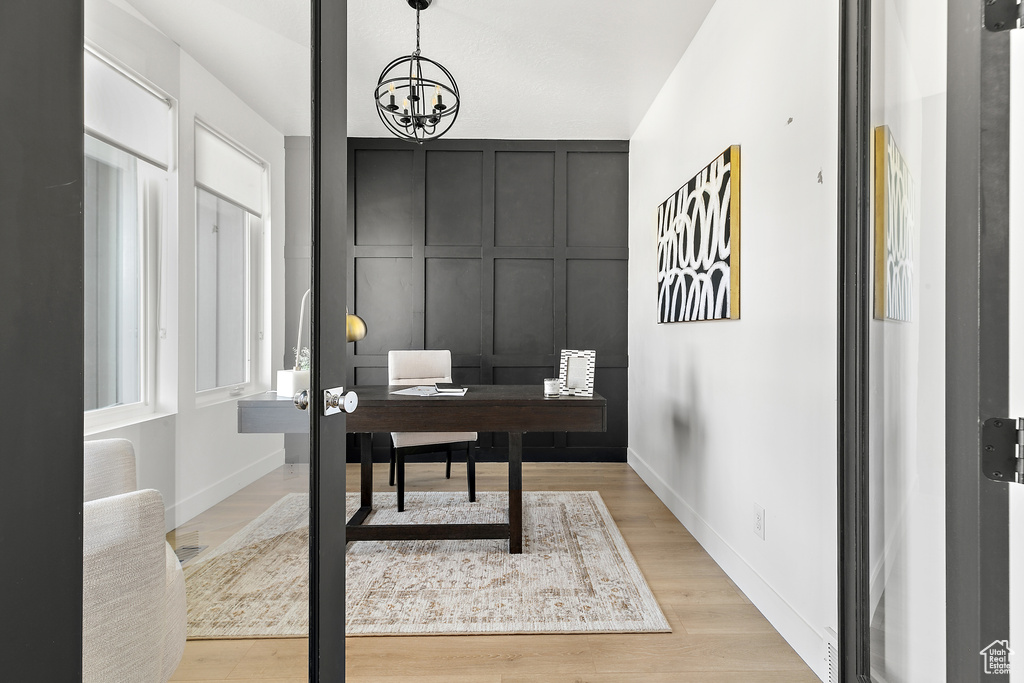Home office featuring light wood-style flooring, a decorative wall, and a chandelier
