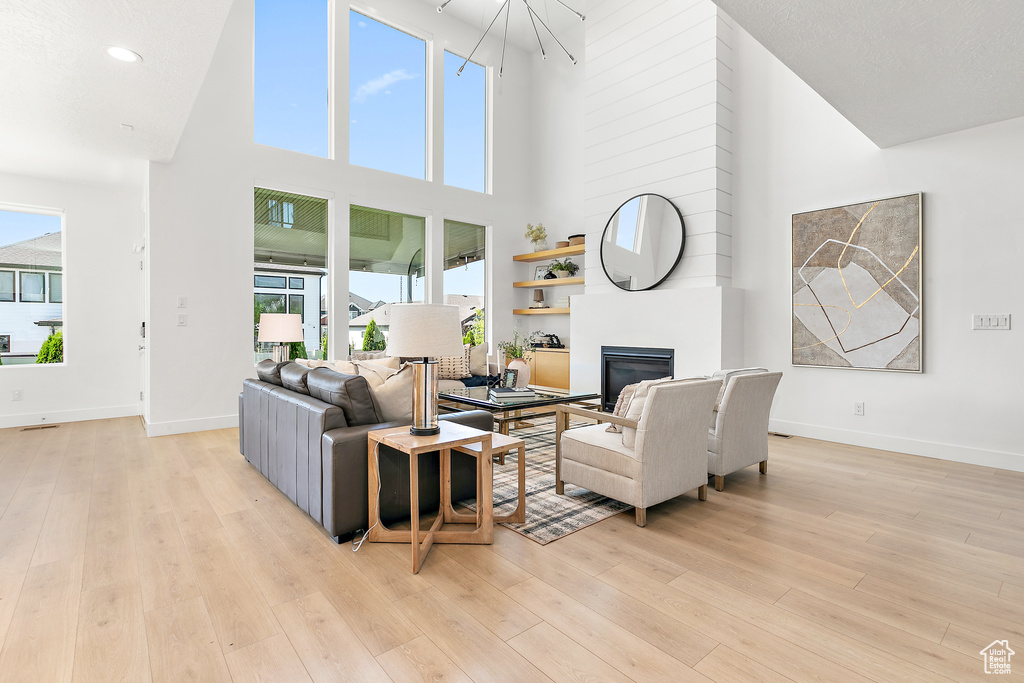 Living area featuring a towering ceiling, a glass covered fireplace, light wood-style flooring, a chandelier, and recessed lighting