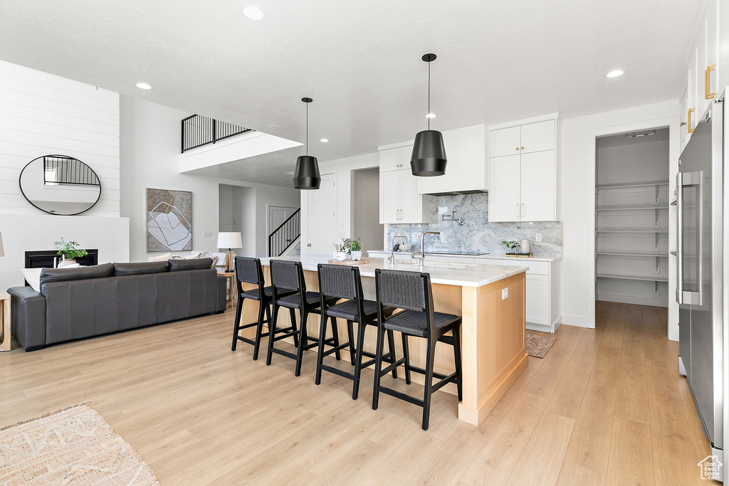 Kitchen featuring open floor plan, light wood-type flooring, backsplash, a breakfast bar, and recessed lighting