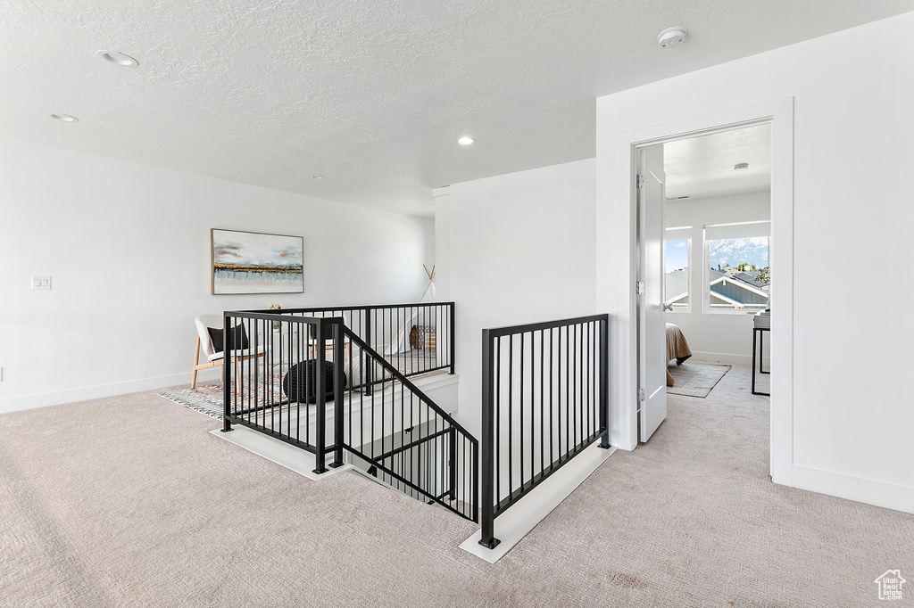 Hallway featuring an upstairs landing, carpet floors, a textured ceiling, and recessed lighting