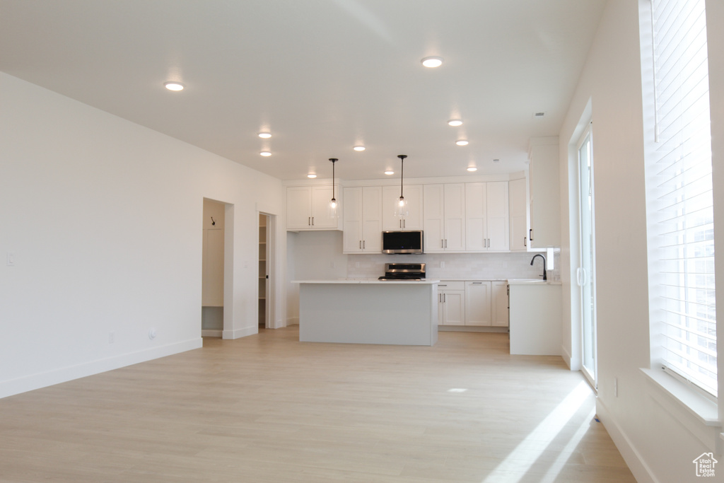 Kitchen with light wood-style flooring, a kitchen island, appliances with stainless steel finishes, and white cabinetry