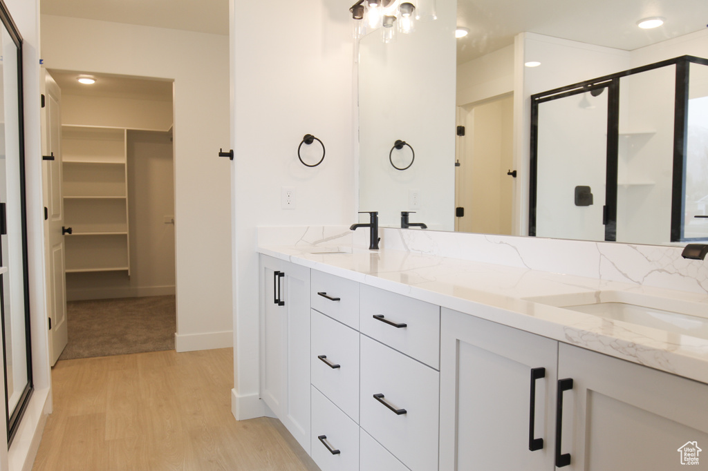 Full bathroom featuring a walk in closet, wood finished floors, a stall shower, and a sink