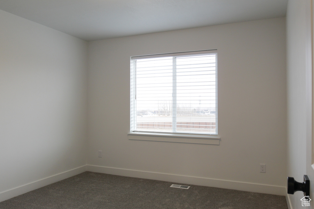 Spare room featuring plenty of natural light, dark colored carpet, and visible vents