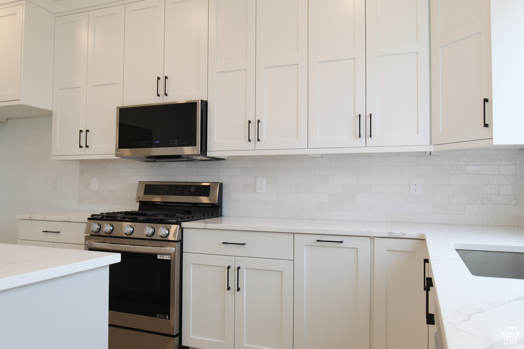Kitchen with white cabinets, tasteful backsplash, light stone counters, and stainless steel appliances