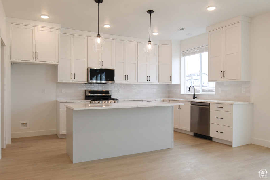 Kitchen with light wood-type flooring, baseboards, white cabinets, and appliances with stainless steel finishes