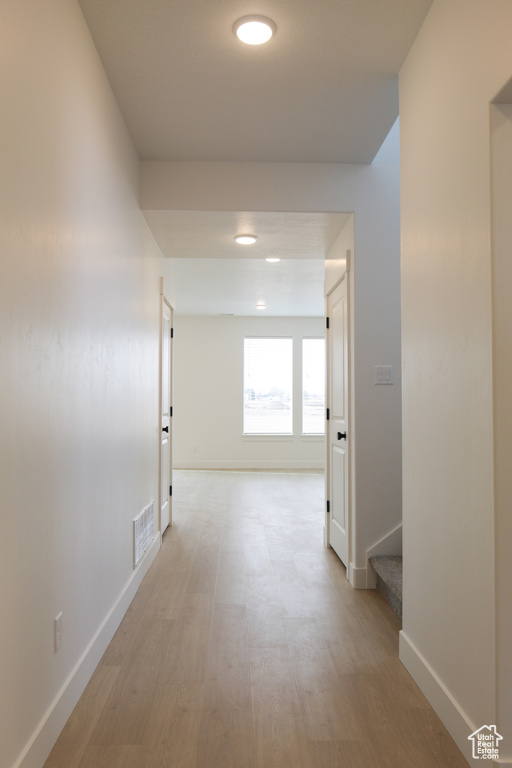 Hallway with baseboards, stairs, visible vents, and light wood-type flooring