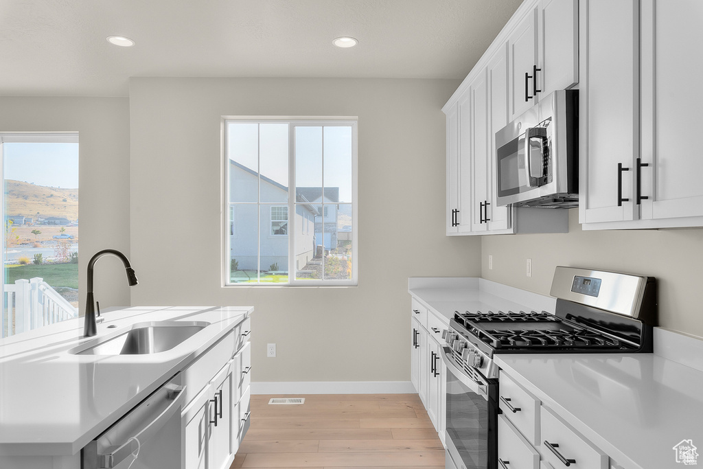 Kitchen featuring visible vents, light wood-style flooring, appliances with stainless steel finishes, light countertops, and a sink