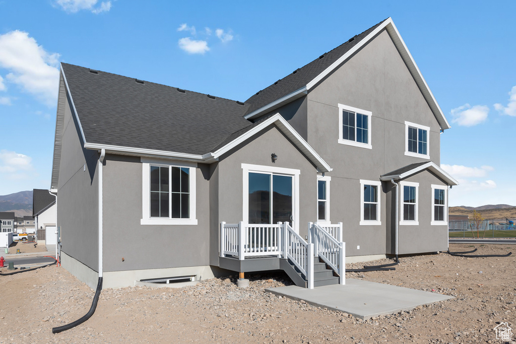 Rear view of house featuring roof with shingles, a mountain view, and stucco siding