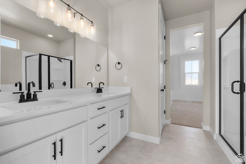 Bathroom featuring double vanity, a stall shower, baseboards, and a sink