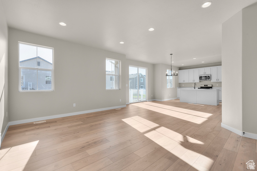 Unfurnished living room featuring light wood-style floors, recessed lighting, baseboards, and an inviting chandelier