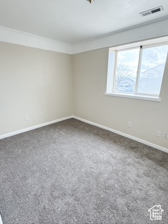 Unfurnished room featuring crown molding, visible vents, dark carpet, and baseboards