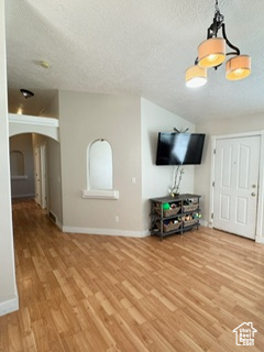 Unfurnished living room featuring arched walkways, a textured ceiling, light wood-style flooring, baseboards, and vaulted ceiling