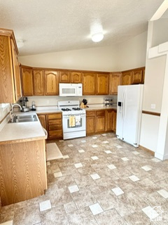 Kitchen with white appliances, brown cabinetry, lofted ceiling, light countertops, and a sink