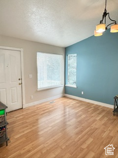 Entryway with lofted ceiling, light wood finished floors, baseboards, and a textured ceiling