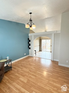 Unfurnished living room with arched walkways, a textured ceiling, a chandelier, baseboards, and light wood finished floors
