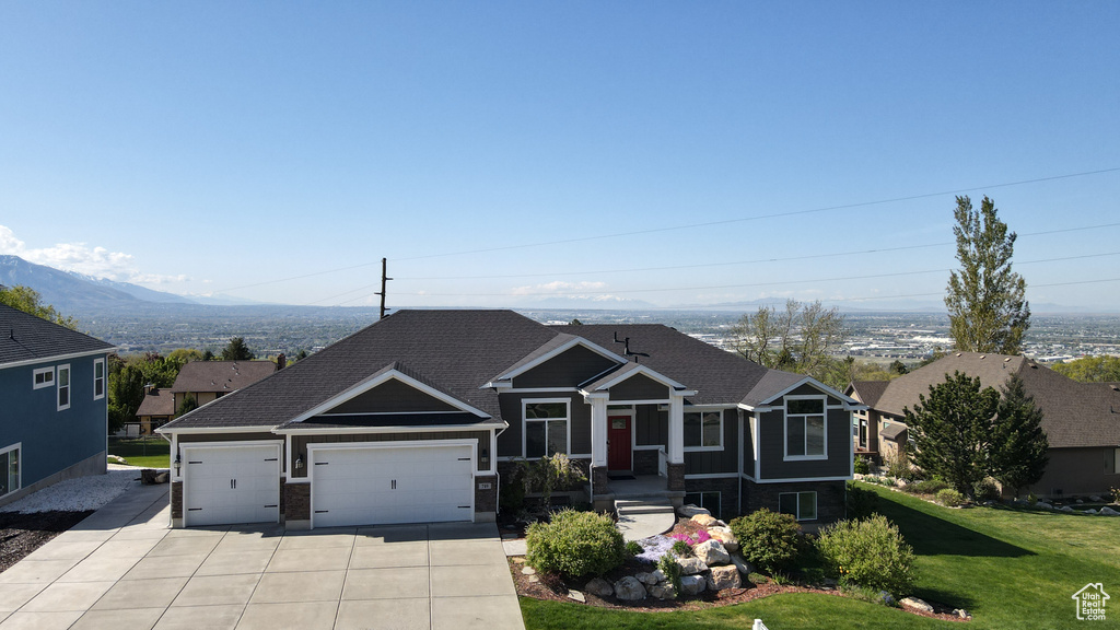 View of front of property featuring a shingled roof, an attached garage, a front lawn, a mountain view, and driveway