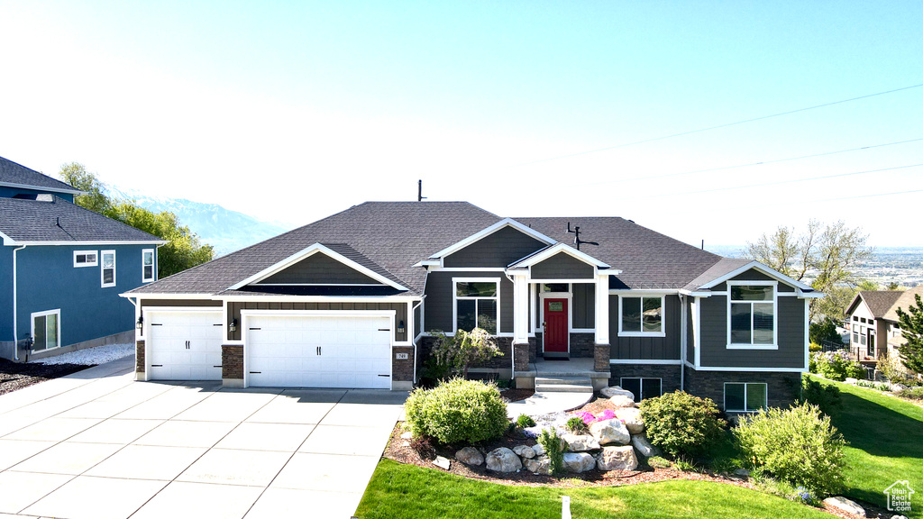 View of front of home featuring an attached garage, a front lawn, stone siding, a mountain view, and driveway