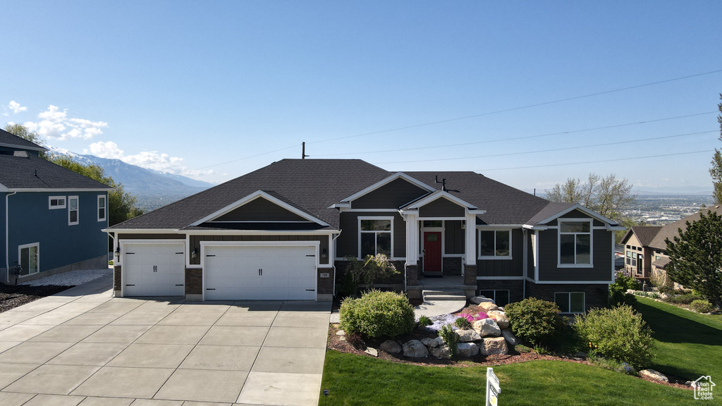 Craftsman house featuring driveway, a garage, a mountain view, a front lawn, and a shingled roof