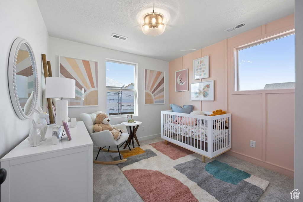 Bedroom with a textured ceiling, light colored carpet, and a nursery area