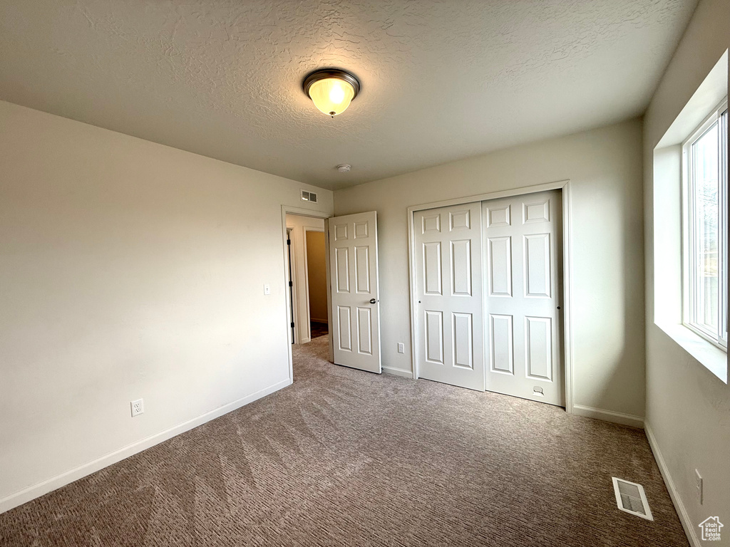 Unfurnished bedroom featuring a textured ceiling, visible vents, baseboards, a closet, and carpet