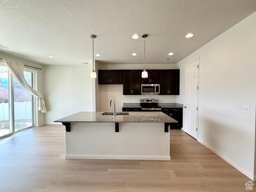 Kitchen with appliances with stainless steel finishes, light wood-type flooring, stone counters, and a sink