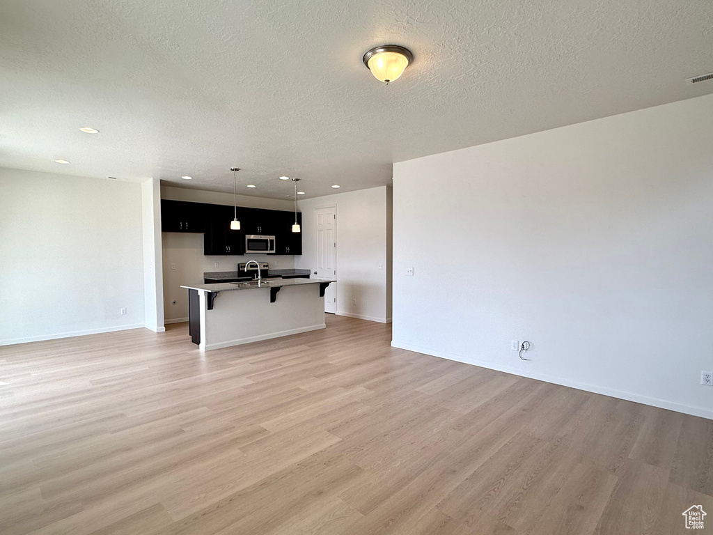 Unfurnished living room with light wood finished floors, baseboards, a textured ceiling, a sink, and recessed lighting