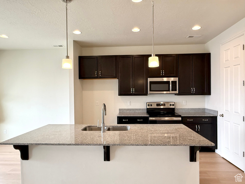 Kitchen featuring dark brown cabinetry, appliances with stainless steel finishes, a kitchen breakfast bar, and a sink