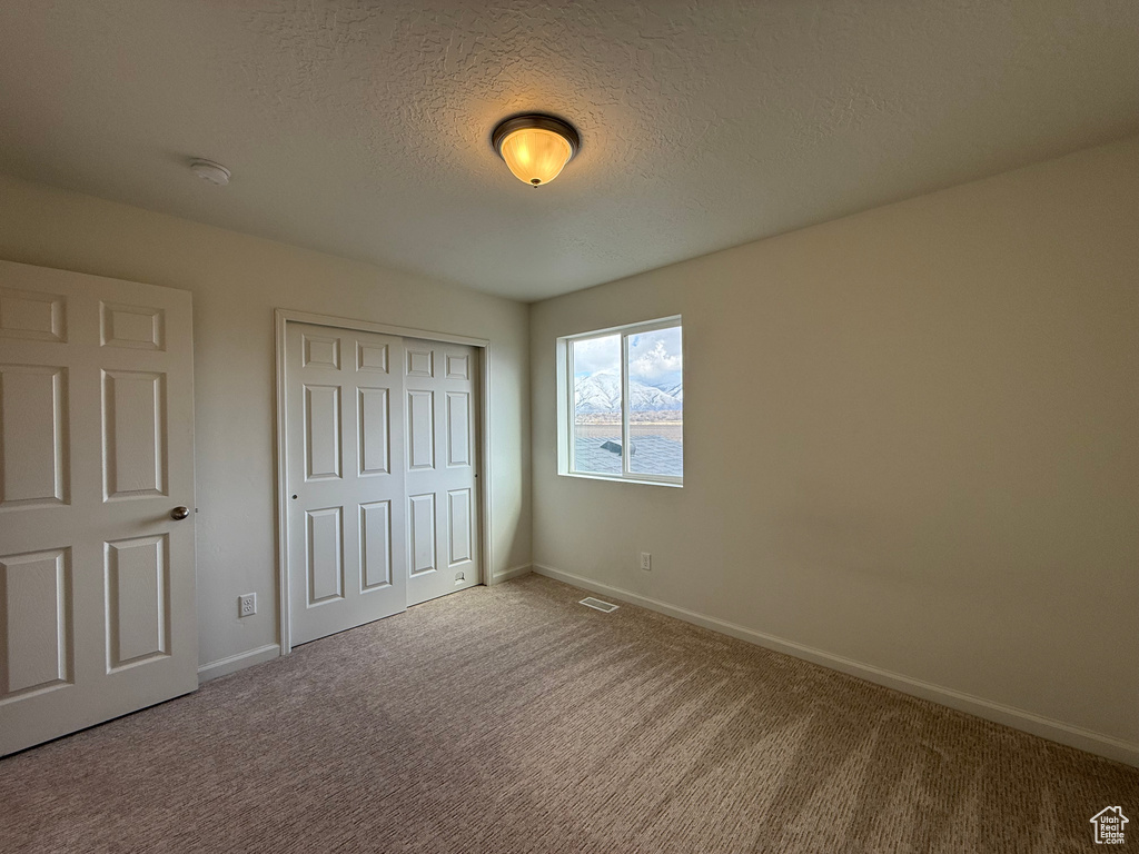 Unfurnished bedroom with carpet, a closet, visible vents, a textured ceiling, and baseboards