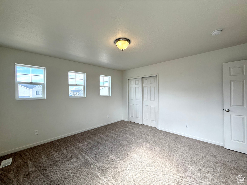 Unfurnished bedroom with dark colored carpet, a closet, visible vents, and baseboards