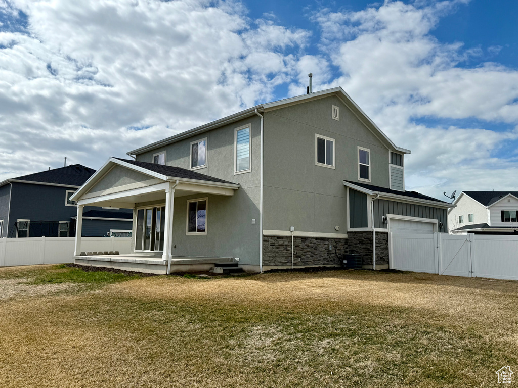 Back of property featuring stone siding, a gate, fence, and a lawn