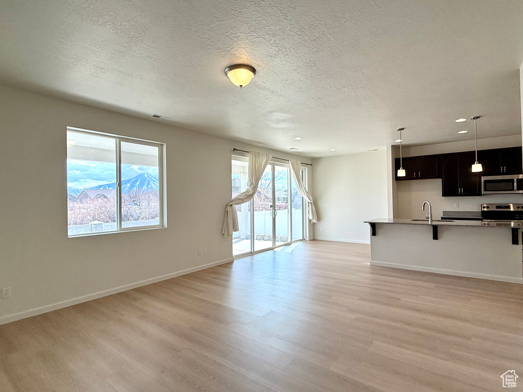 Unfurnished living room featuring a sink, light wood-style flooring, baseboards, and a textured ceiling