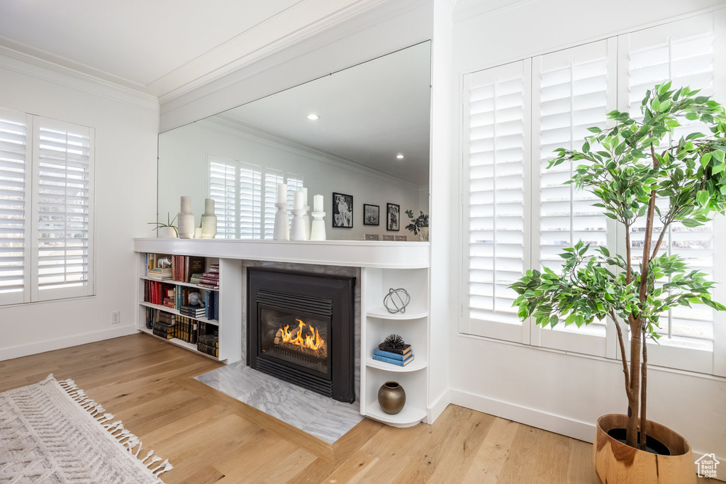 Living area featuring crown molding, healthy amount of natural light, wood finished floors, and a fireplace with flush hearth