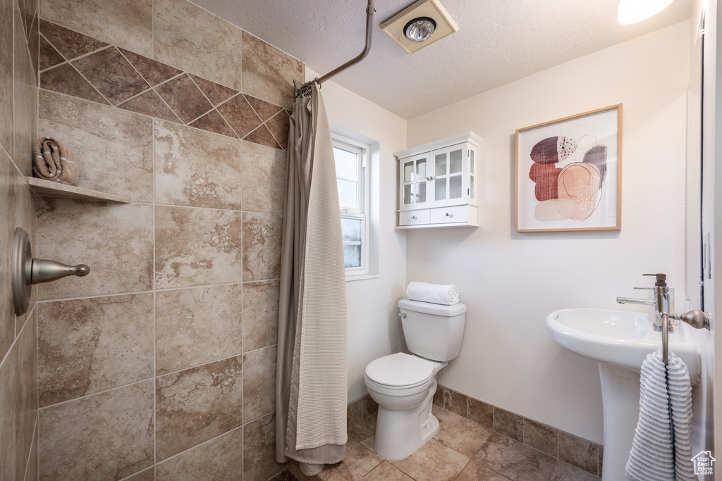 Full bath with a tile shower, toilet, baseboards, and a sink