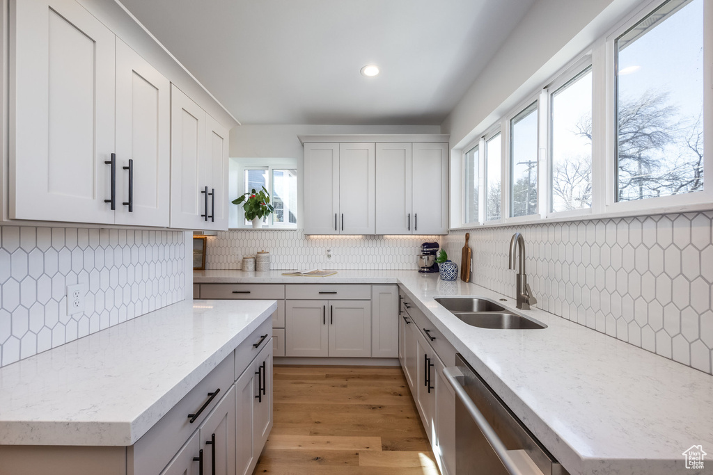 Kitchen with a sink, stainless steel dishwasher, backsplash, light stone counters, and recessed lighting