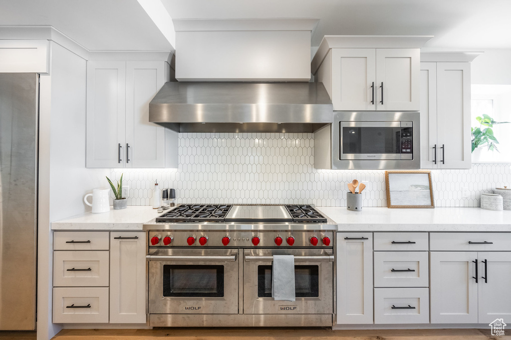 Kitchen featuring stainless steel appliances, wall chimney exhaust hood, decorative backsplash, and white cabinetry