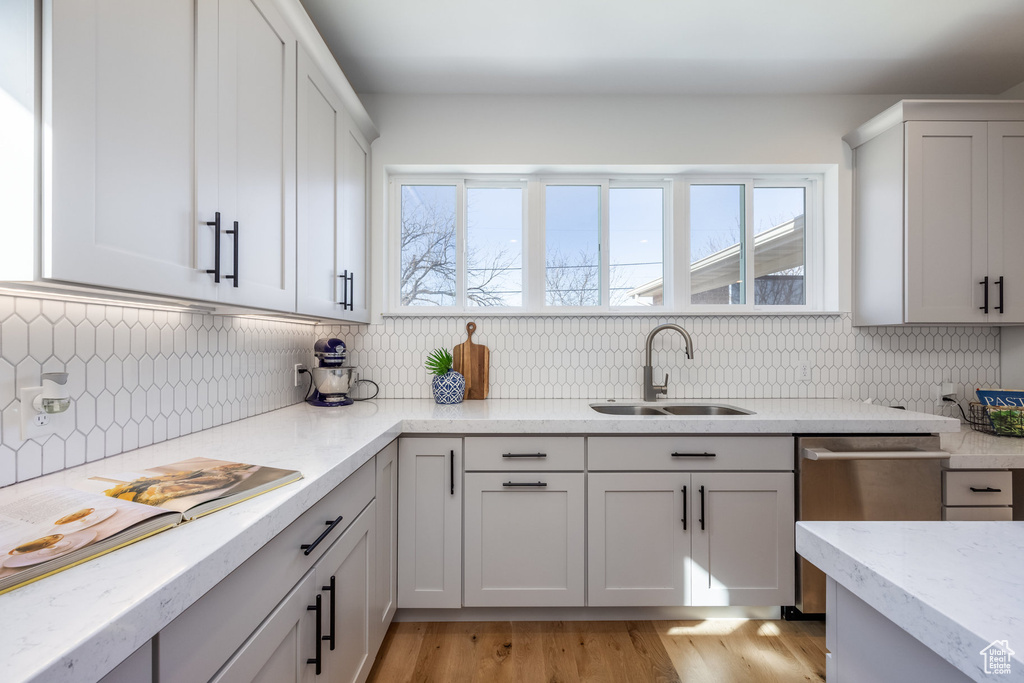 Kitchen with a sink, stainless steel dishwasher, tasteful backsplash, and light stone counters