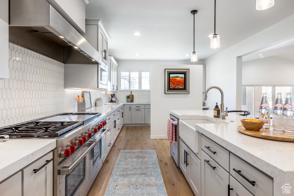 Kitchen featuring wall chimney exhaust hood, appliances with stainless steel finishes, a sink, tasteful backsplash, and light wood-style floors