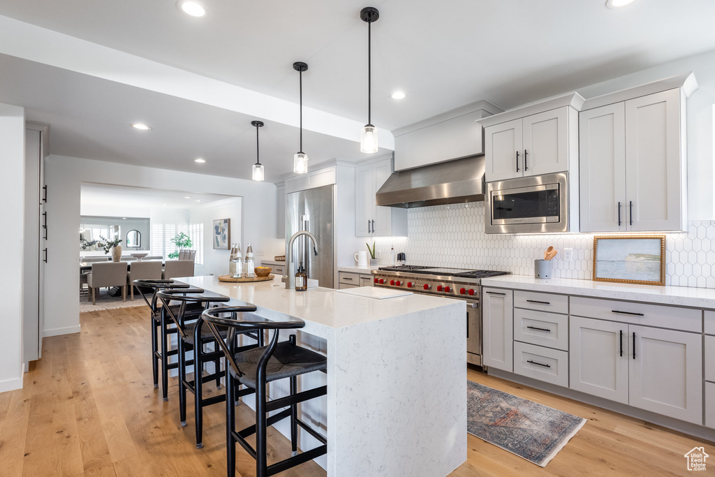 Kitchen featuring premium appliances, wall chimney range hood, a breakfast bar area, backsplash, and recessed lighting