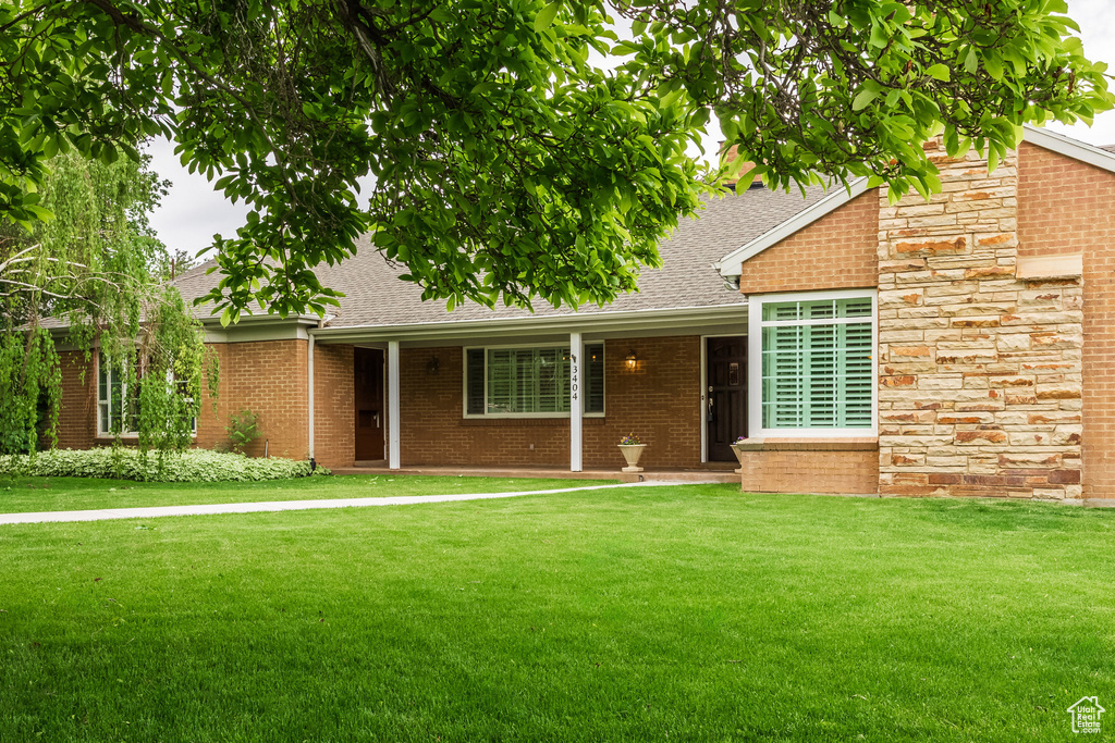 View of front facade with roof with shingles, a front yard, and brick siding