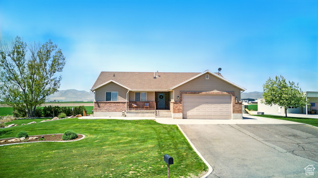 Single story home with driveway, brick siding, a mountain view, a garage, and a front lawn