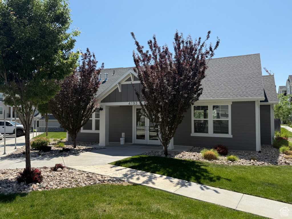 View of property hidden behind natural elements featuring roof with shingles, a front yard, and french doors