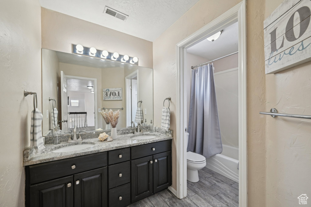 Bathroom with toilet, double vanity, wood finished floors, and shower / bath combo