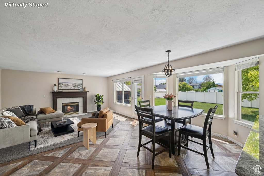 Dining area with a textured ceiling, a tile fireplace, baseboards, and a chandelier