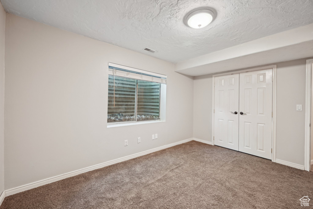 Unfurnished bedroom with carpet, a textured ceiling, baseboards, and a closet